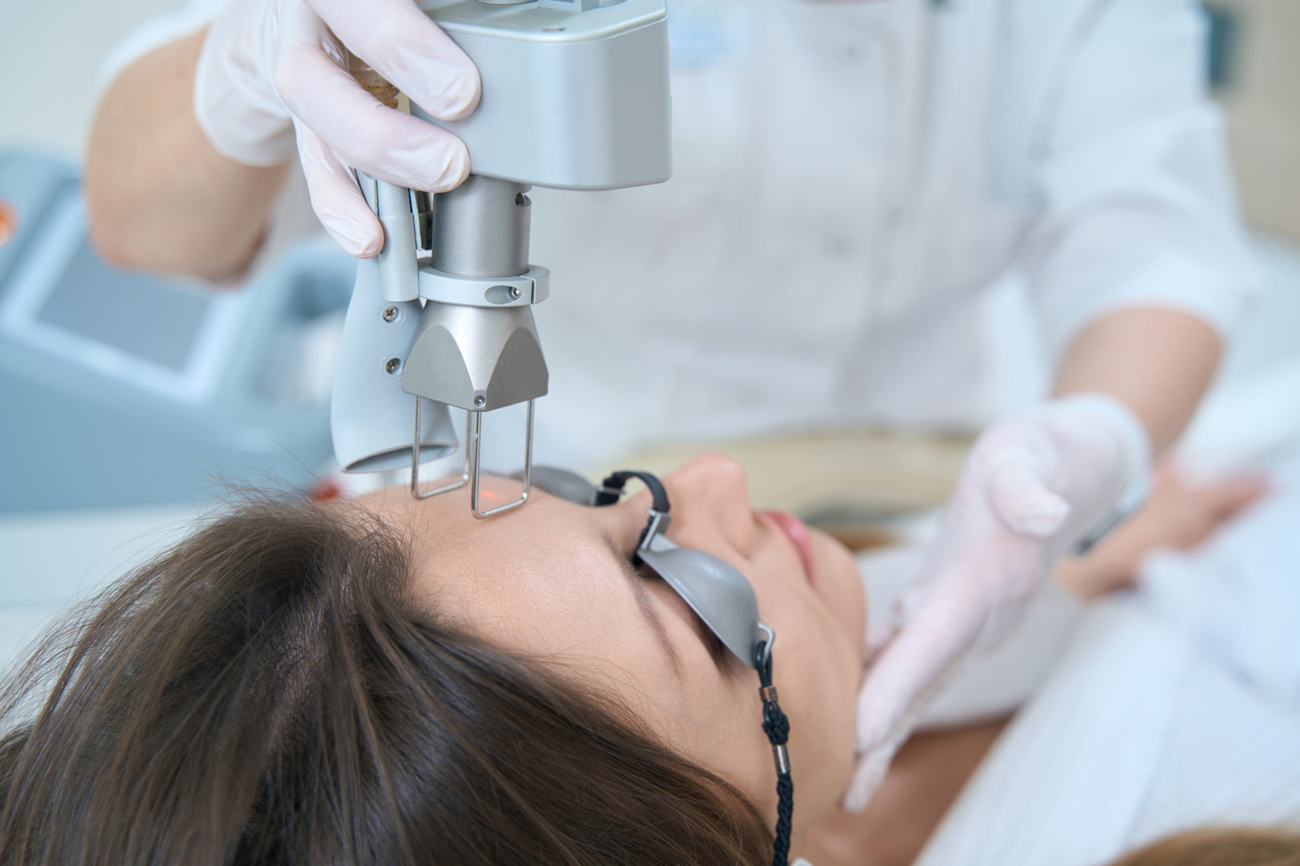 Woman at a medical and cosmetology center undergoing a procedure for removing tumors with a laser in the forehead